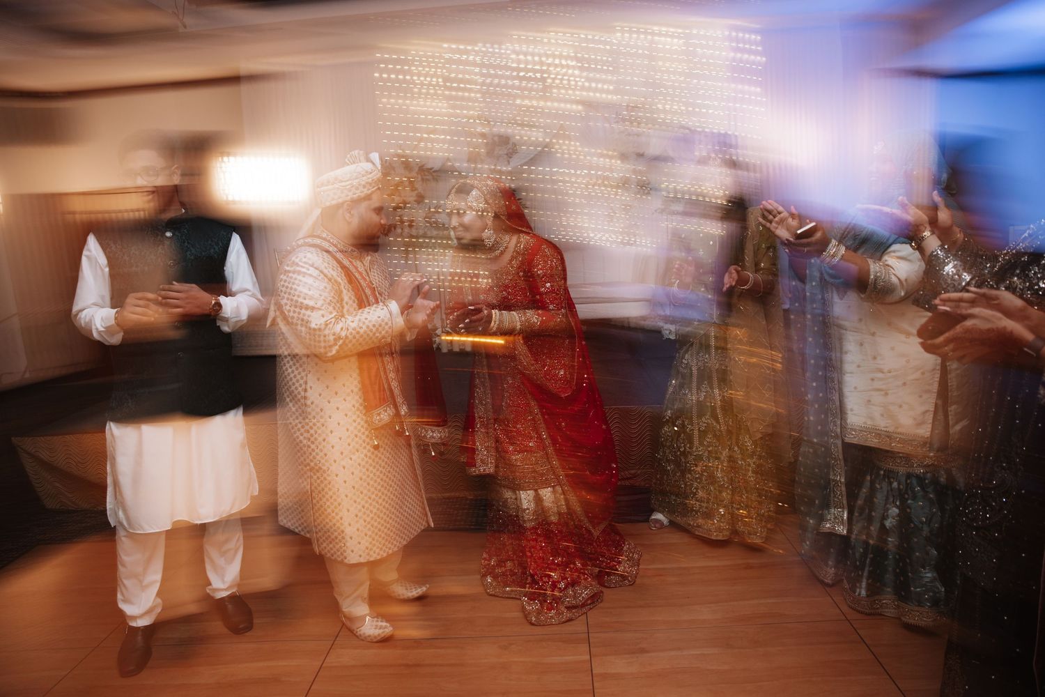Motion blur photo of Indian wedding celebration with bride in red lehenga dancing with guests.