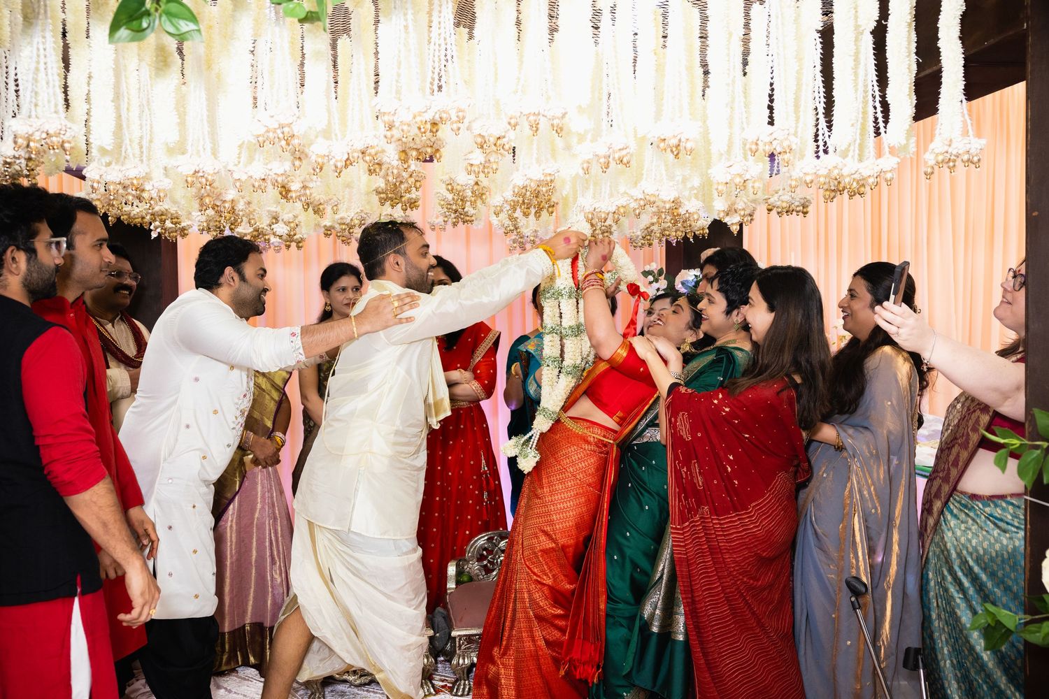 Joyful Indian wedding celebration with guests in colorful traditional attire under floral canopy decorations.