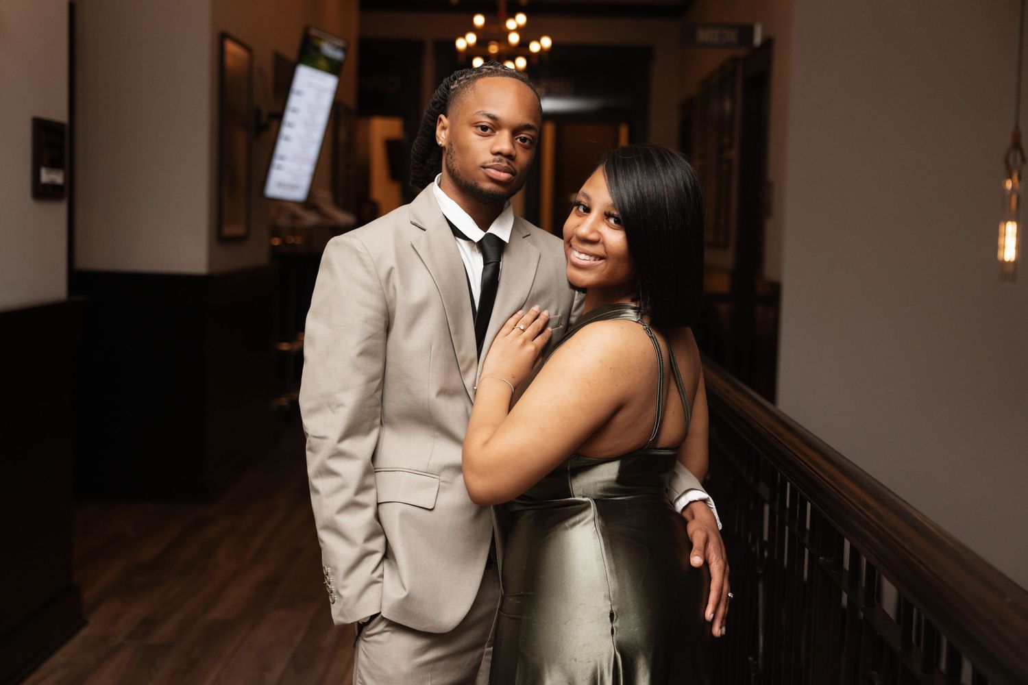 Elegant couple posing together in a dimly lit wedding venue hallway in formal attire.