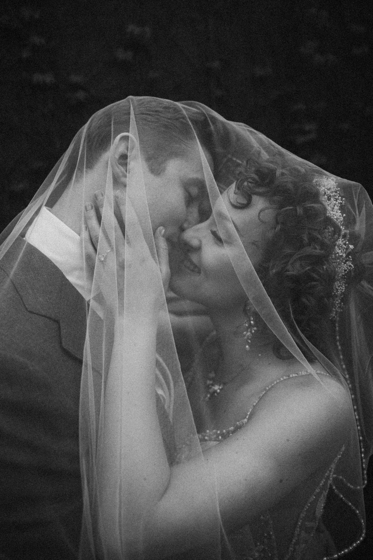 Black and white photo of bride and groom sharing romantic moment under wedding veil.