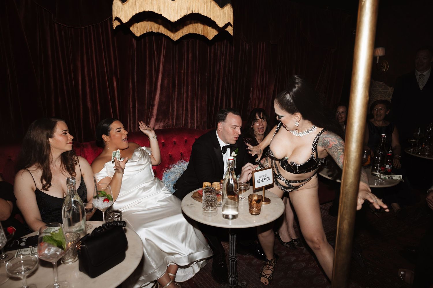 Bride and groom enjoy entertainment with guests at a sophisticated dark lounge wedding reception.