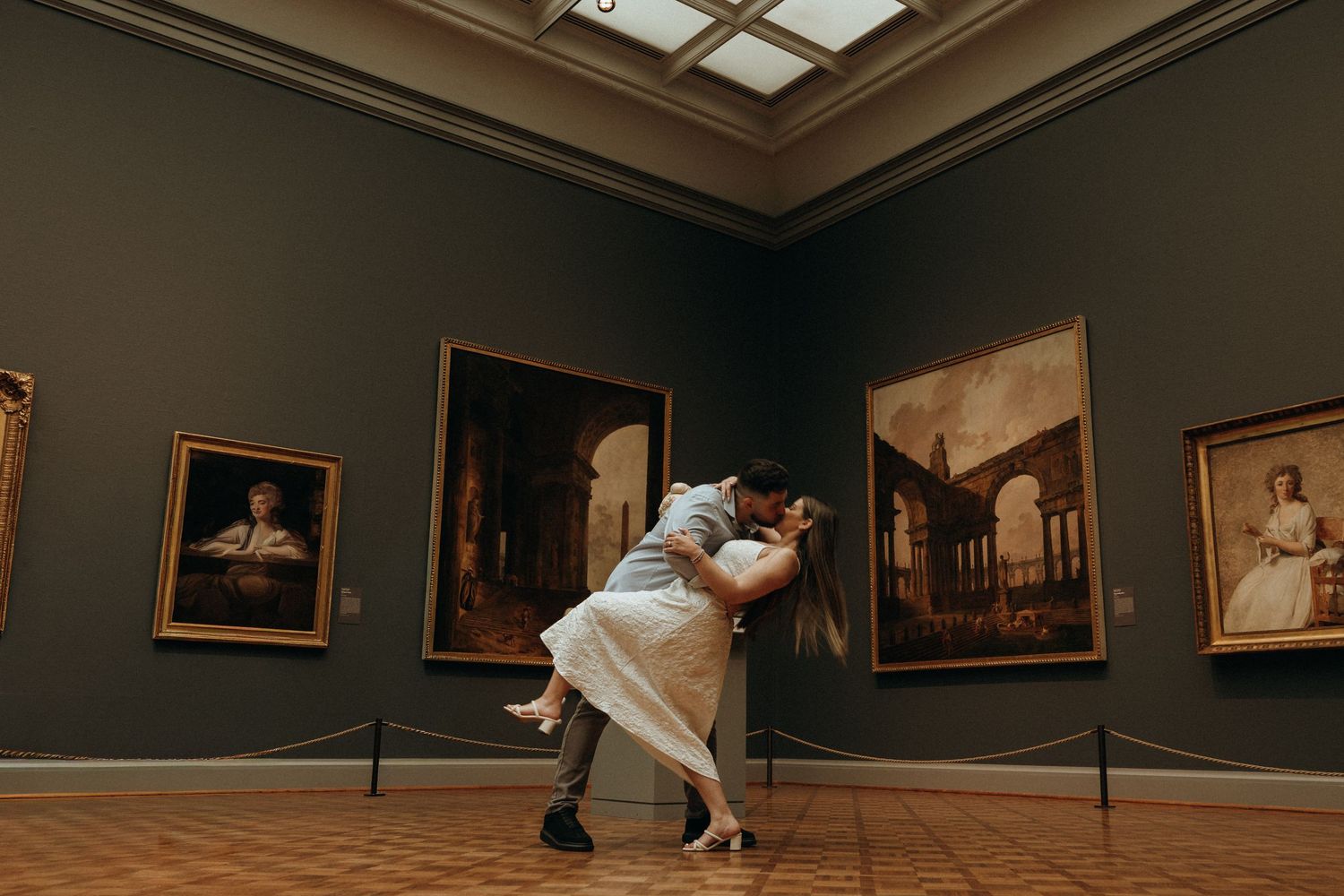 Couple sharing a romantic dip and embrace in a classic art museum gallery with paintings.