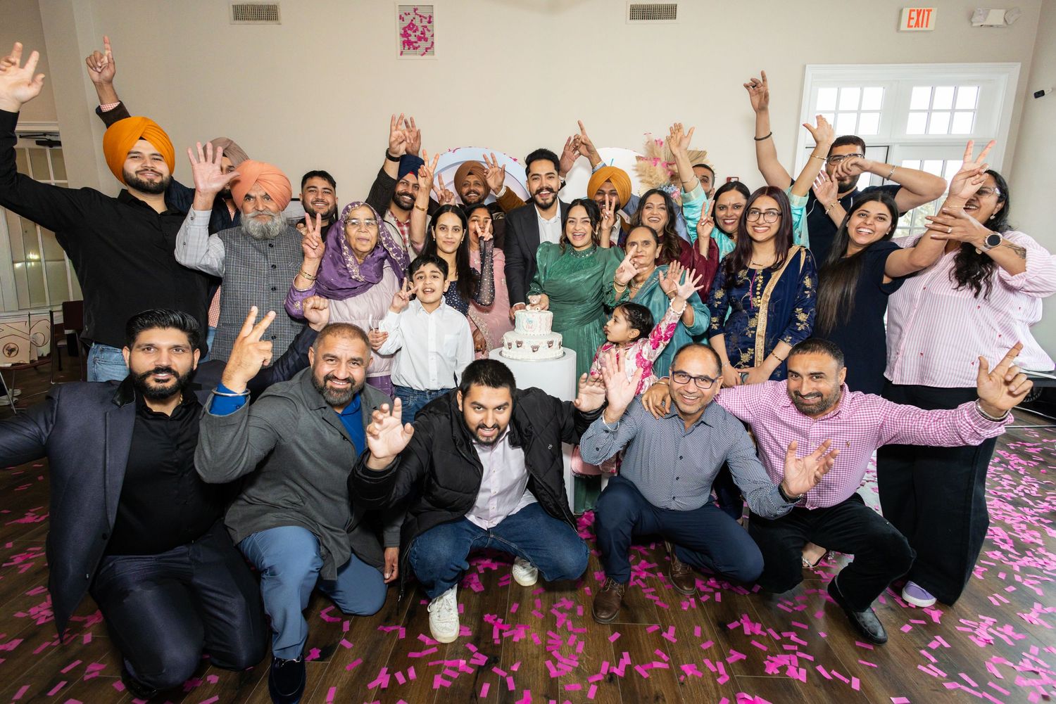 Large group of joyful South Asian guests celebrate at a gender reveal party with confetti and cheering.