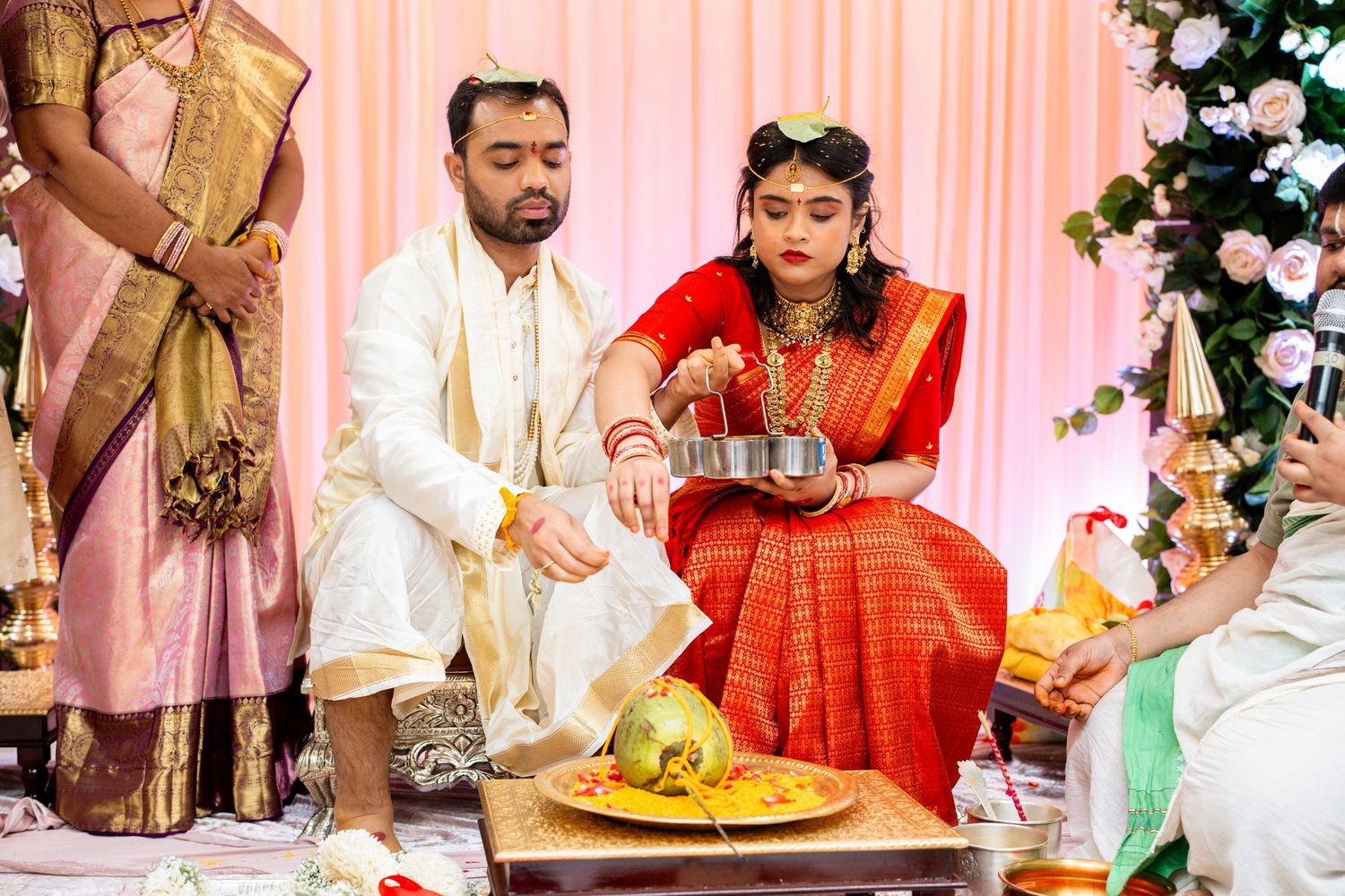 Hindu wedding couple performing traditional water ritual ceremony, bride in red saree with gold jewelry.