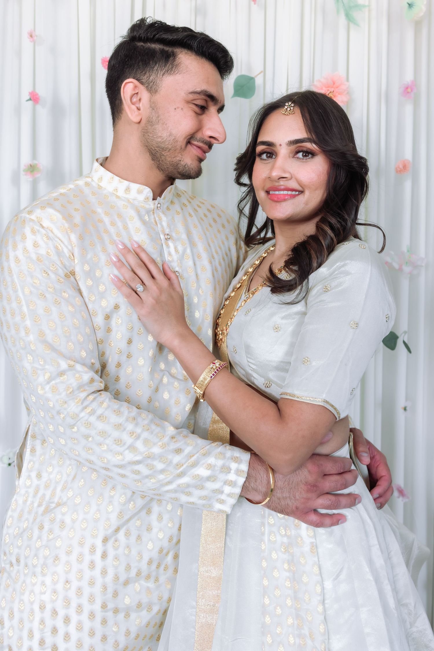 South Asian wedding couple in white and gold traditional outfits sharing a tender moment together.
