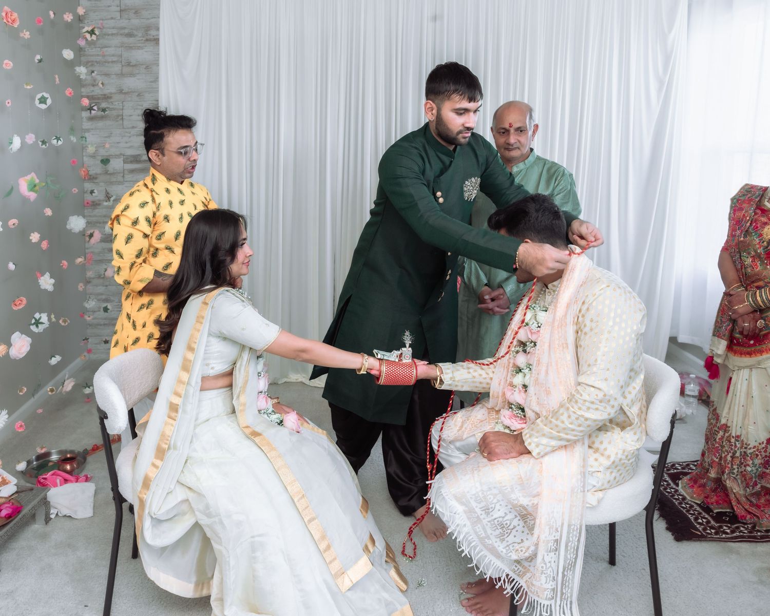 Family members perform a traditional South Asian wedding ritual with the bride in white and groom in cream attire.
