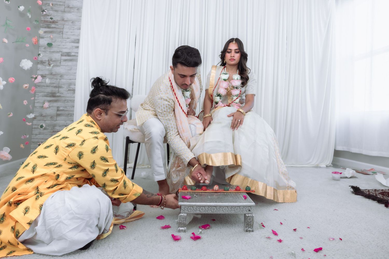 A priest performs a traditional Indian wedding ritual with the bride and groom seated nearby.