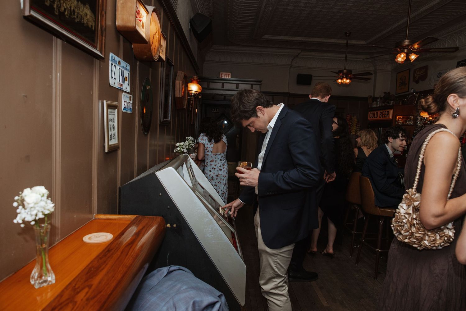 Man in navy blazer uses a vintage jukebox inside a dimly lit rustic bar venue.