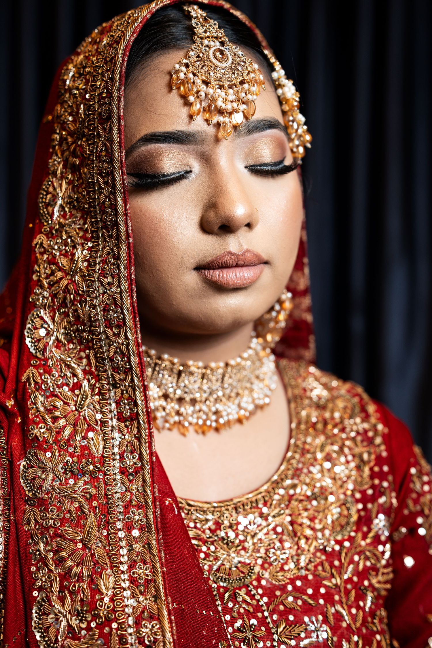 Close-up of a bride wearing traditional Indian gold bridal jewelry and red dupatta with eyes closed.