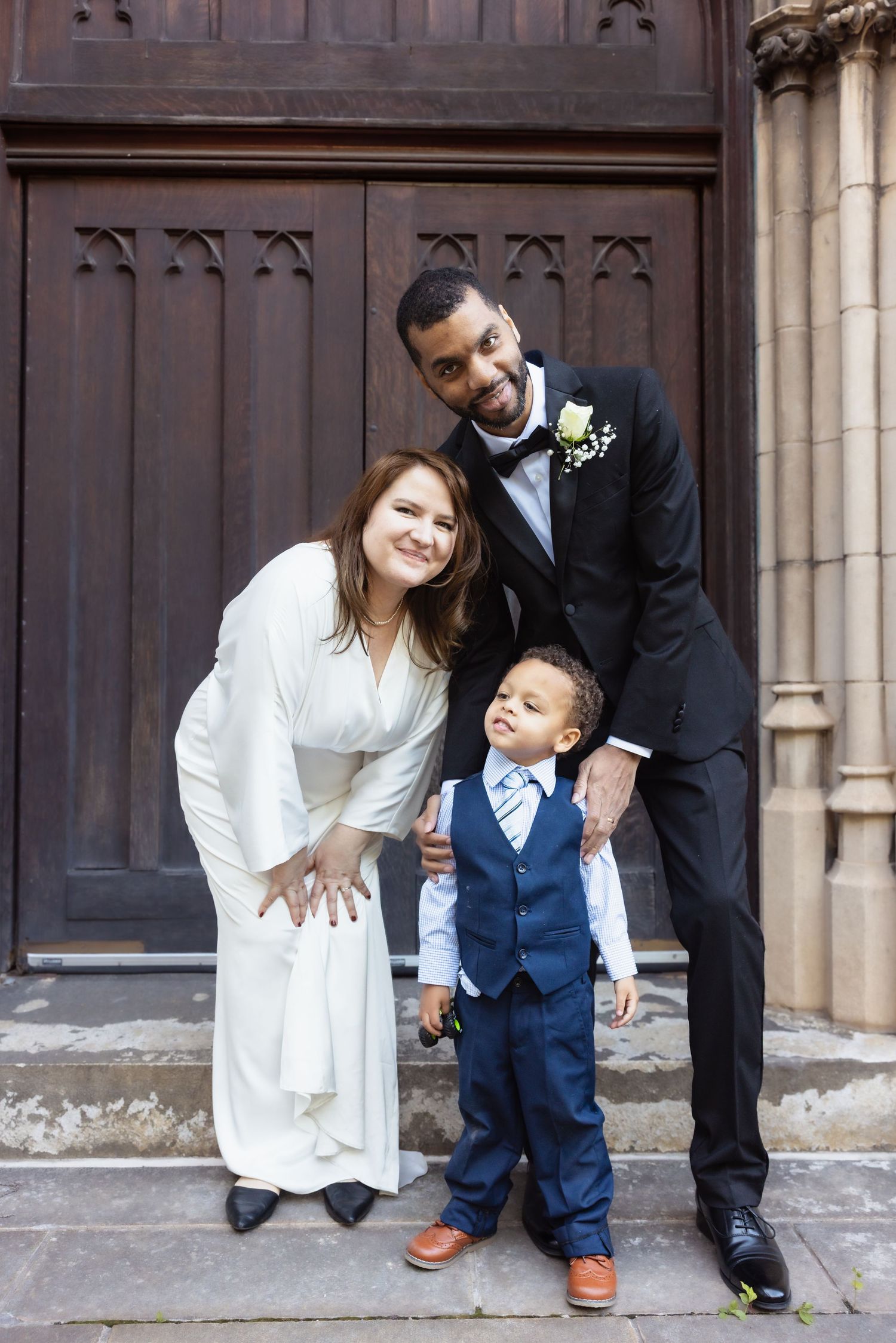 Bride and groom pose with young boy in suit at church entrance.