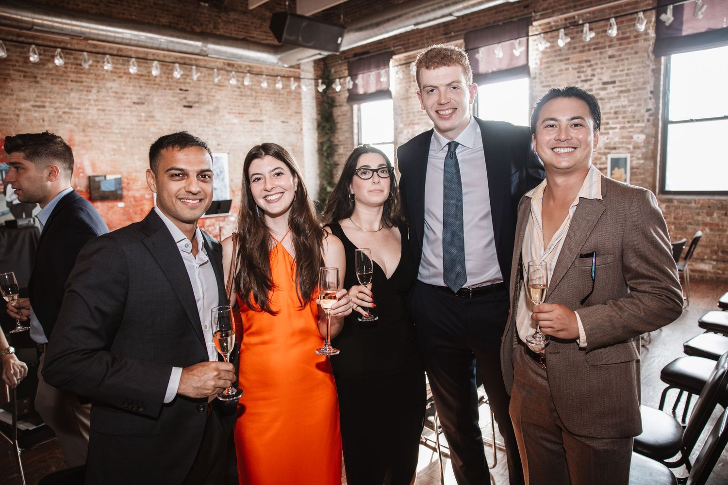 Group of five elegantly dressed guests smiling and holding champagne at a wedding reception.