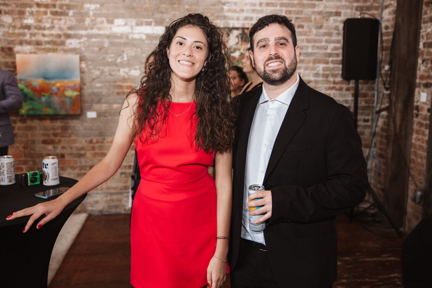 Smiling couple posing together at a casual formal event in a brick-walled venue.