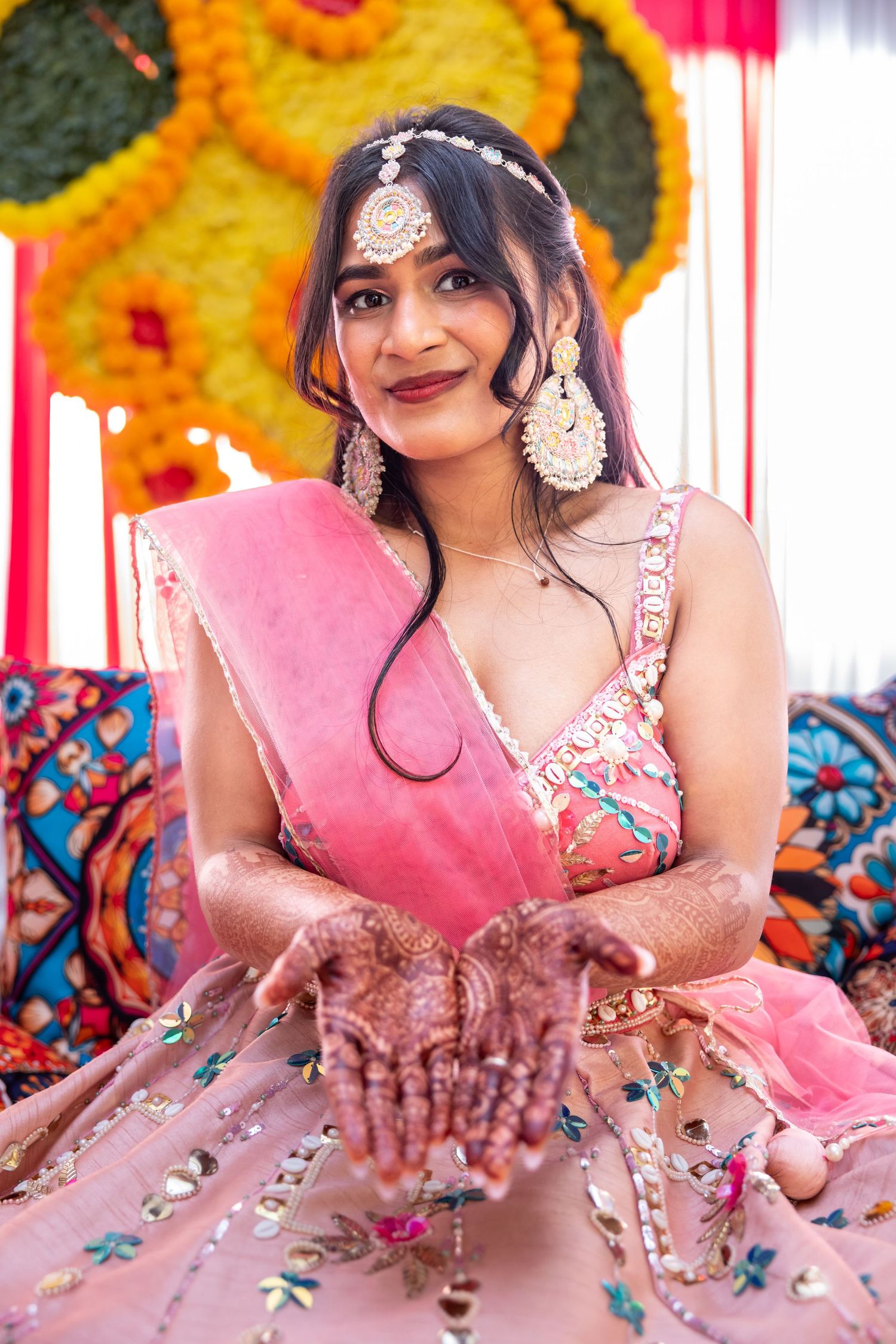 Indian bride in pink lehenga showing intricate mehndi henna designs on hands at traditional mehndi ceremony.