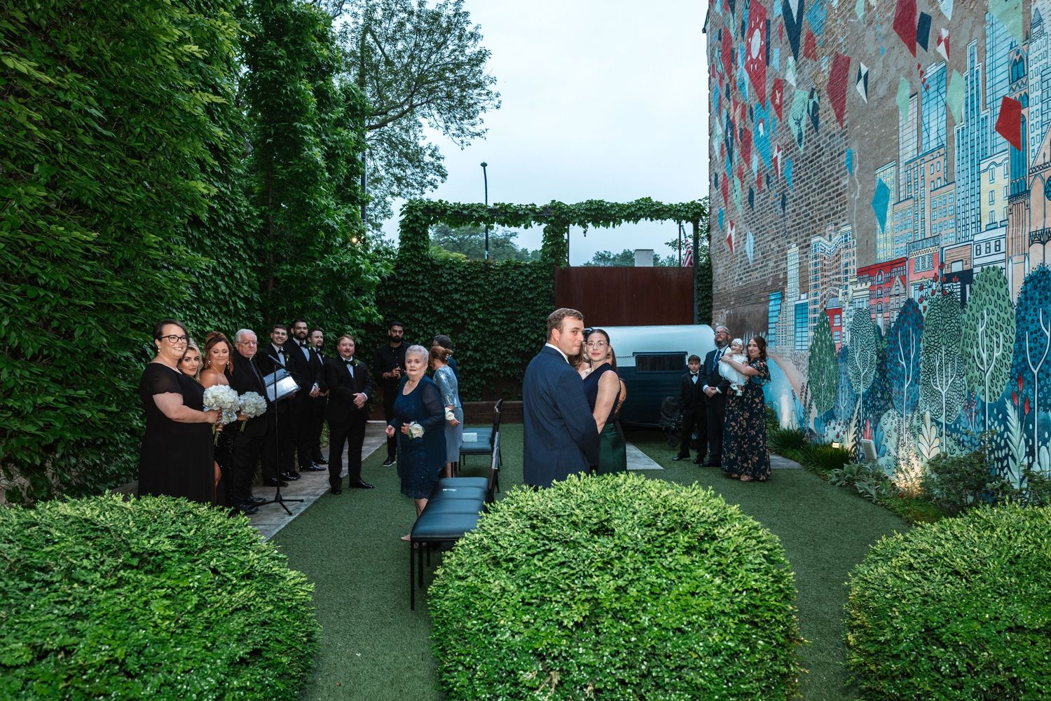 A bride and groom share their first kiss in an outdoor garden ceremony with a colorful mural backdrop.