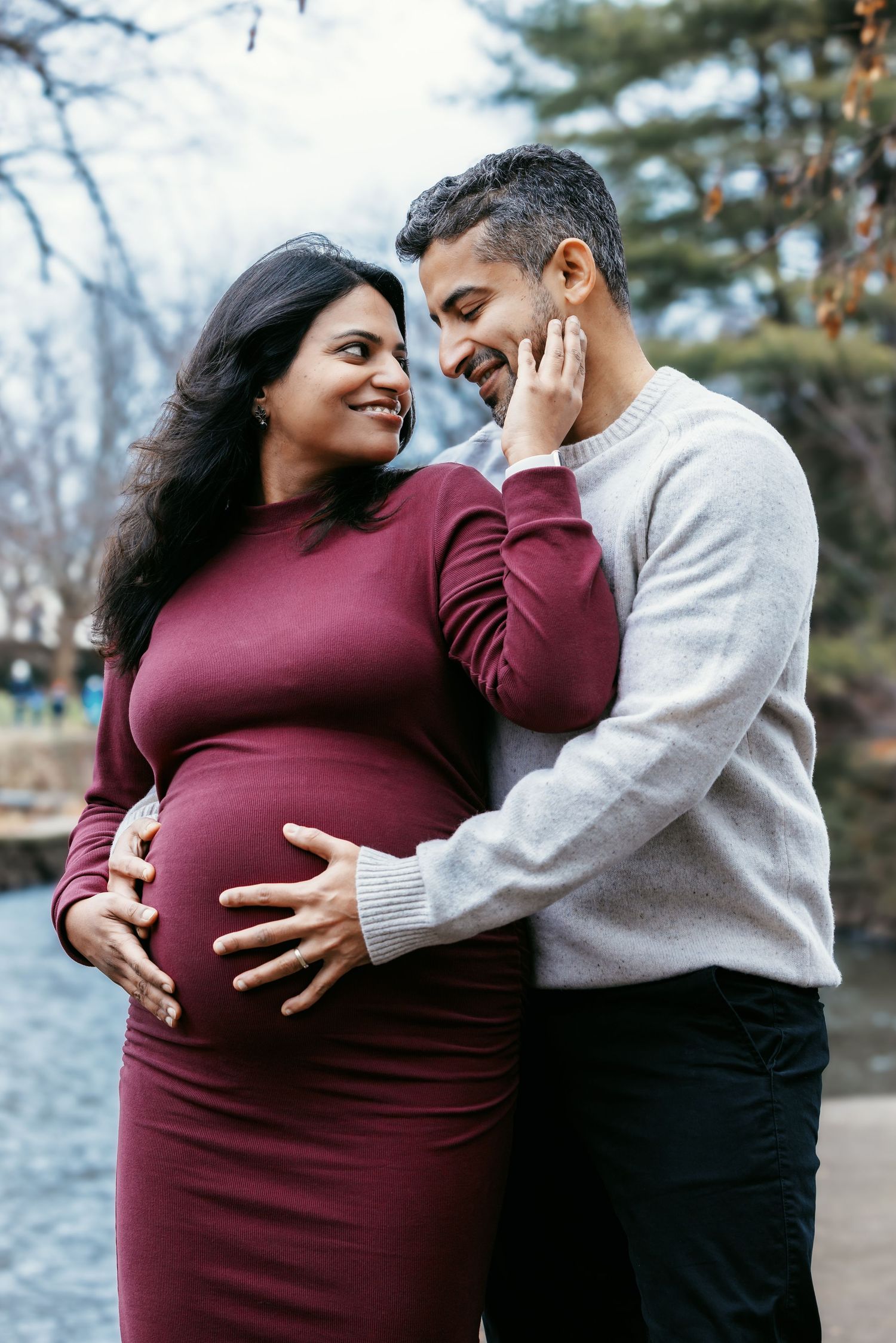 Smiling expectant couple embracing outdoors, man gently touching woman's face during maternity shoot.