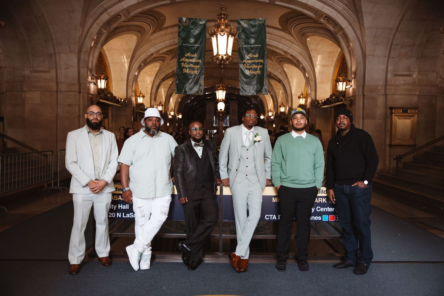 Six men posing together in an ornate building with arched ceilings and decorative banners.