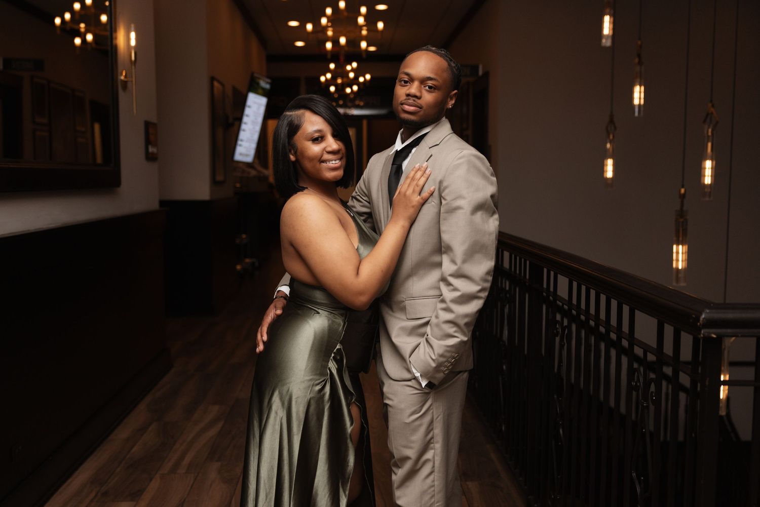 Couple posing elegantly in formal attire in dimly lit venue with string lights.