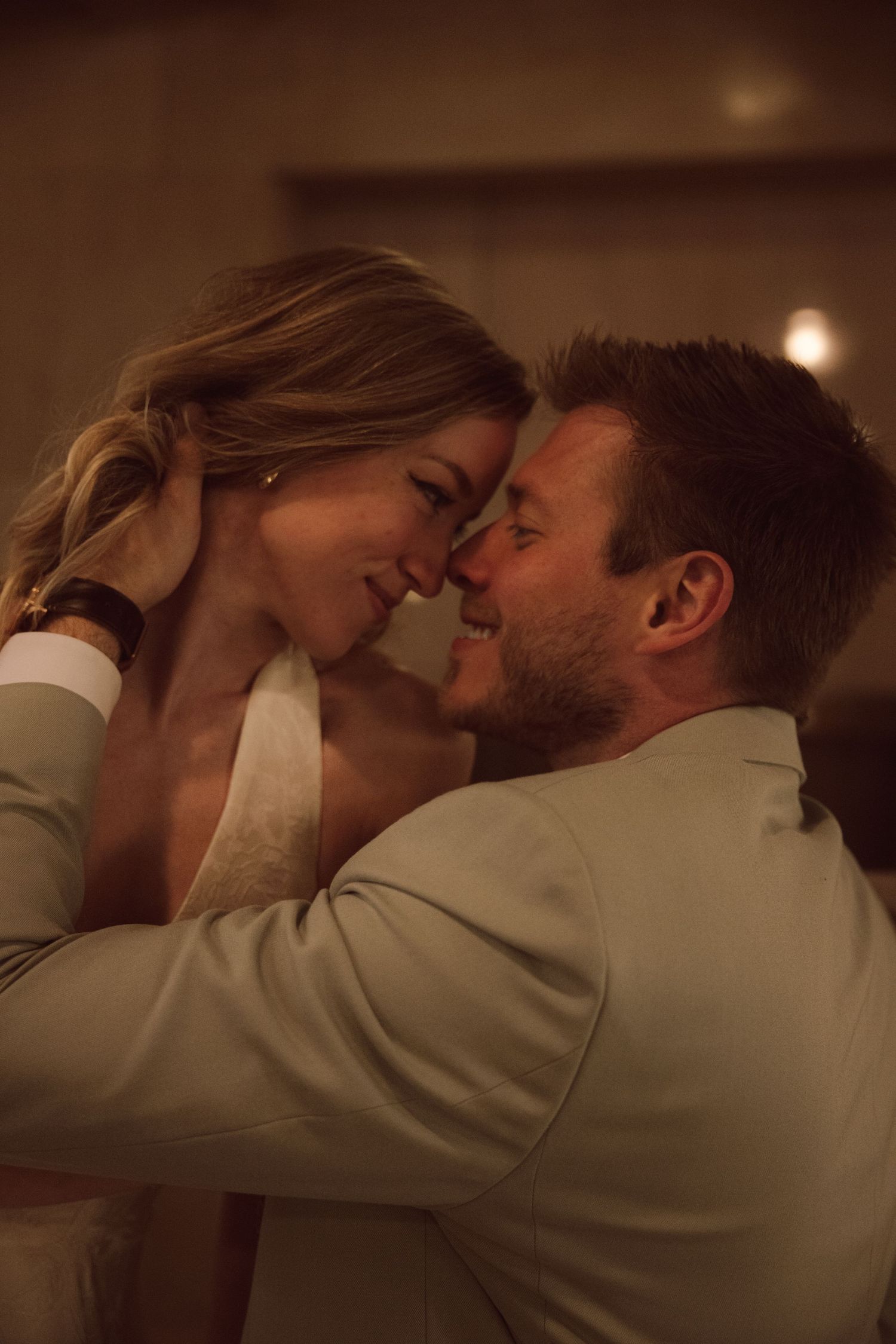 Bride and groom share an intimate moment, touching foreheads and smiling in warm romantic lighting.