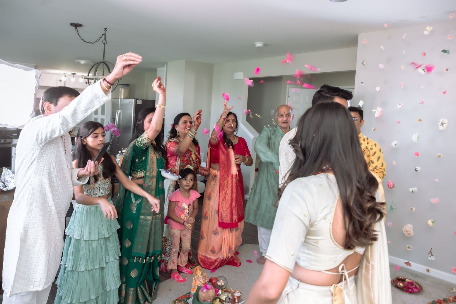 Indian wedding guests celebrating with colorful flower petal toss indoors.