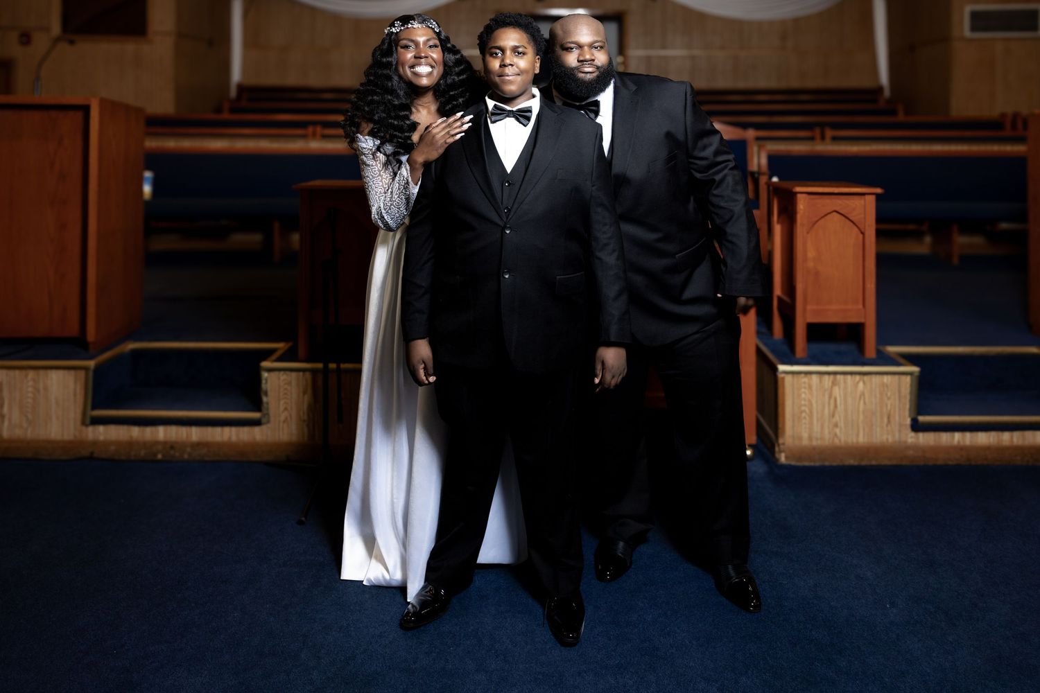 Bride in white gown posing with two guests in black formal attire inside a church.