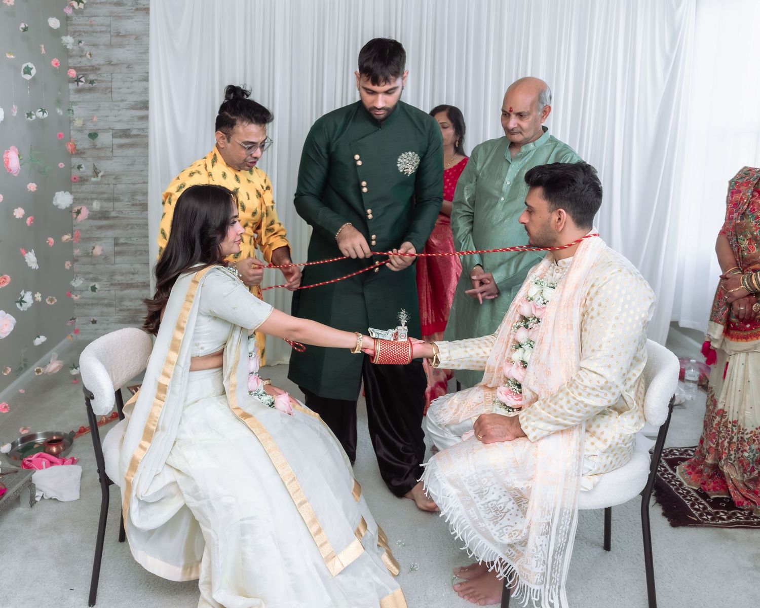 Indian bride and groom seated during traditional Hindu wedding ceremony with family members standing nearby.