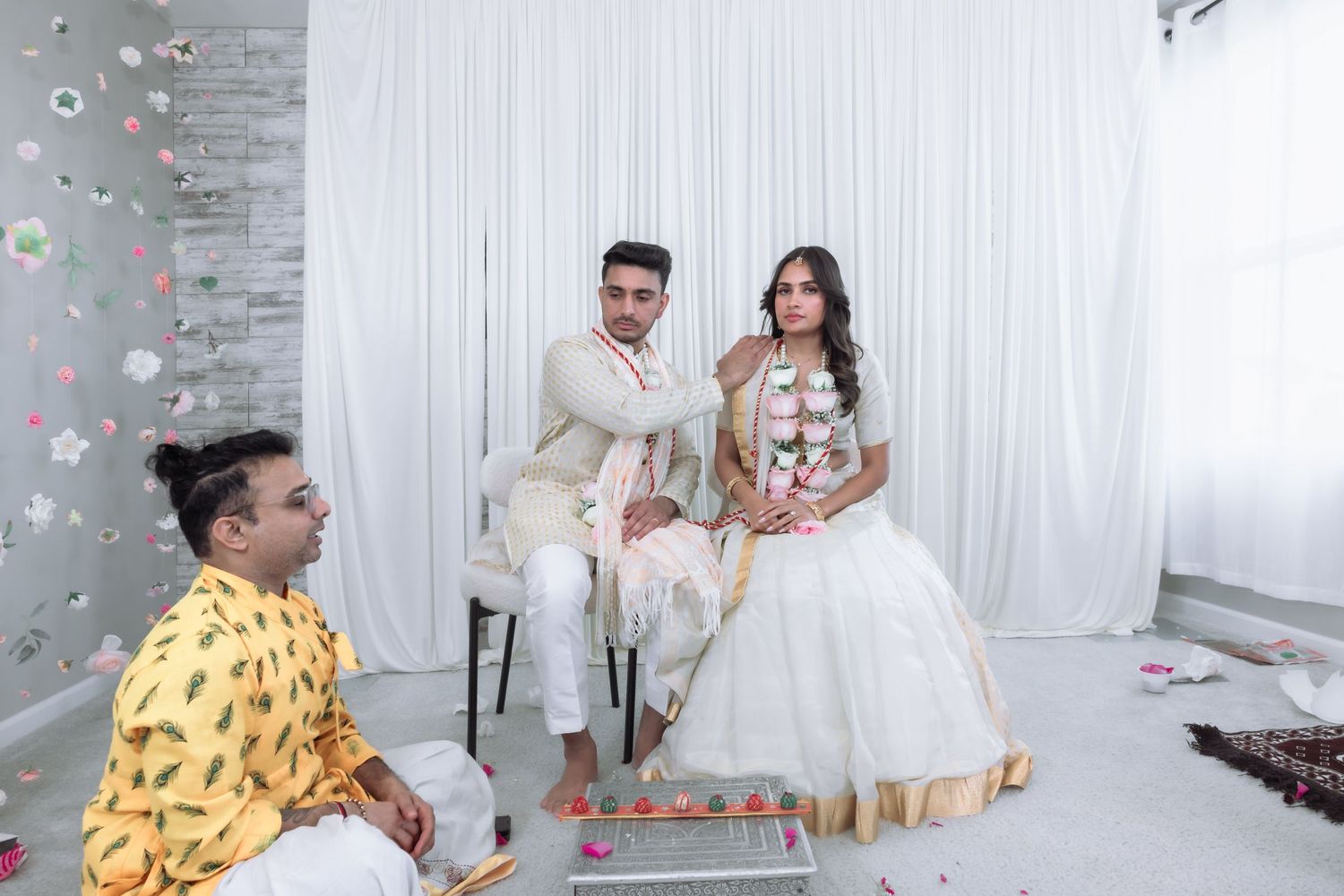 Bride and groom sit together during an Indian wedding ceremony with flower petals falling.