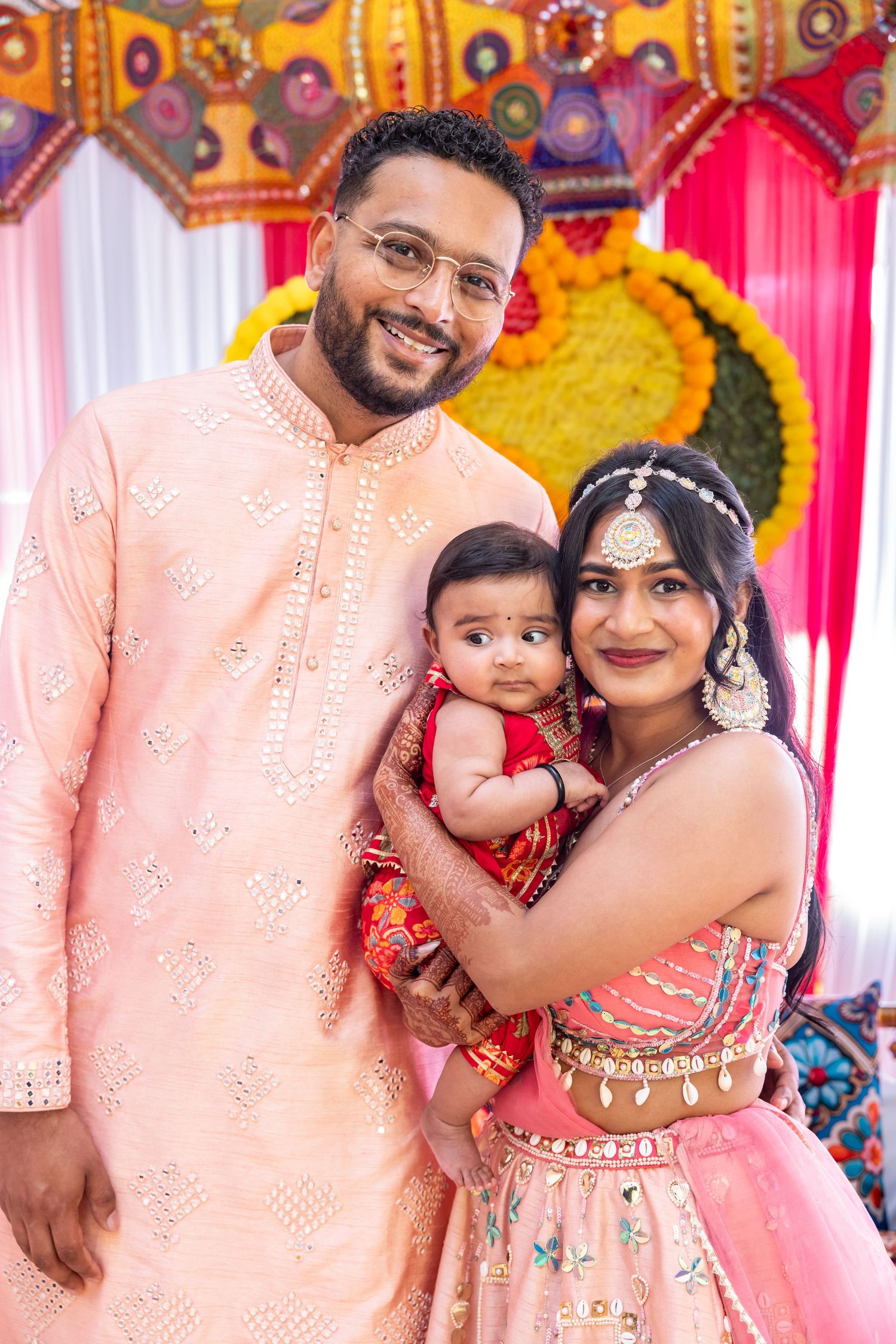 Indian family in pink traditional attire with baby at decorated cultural celebration.
