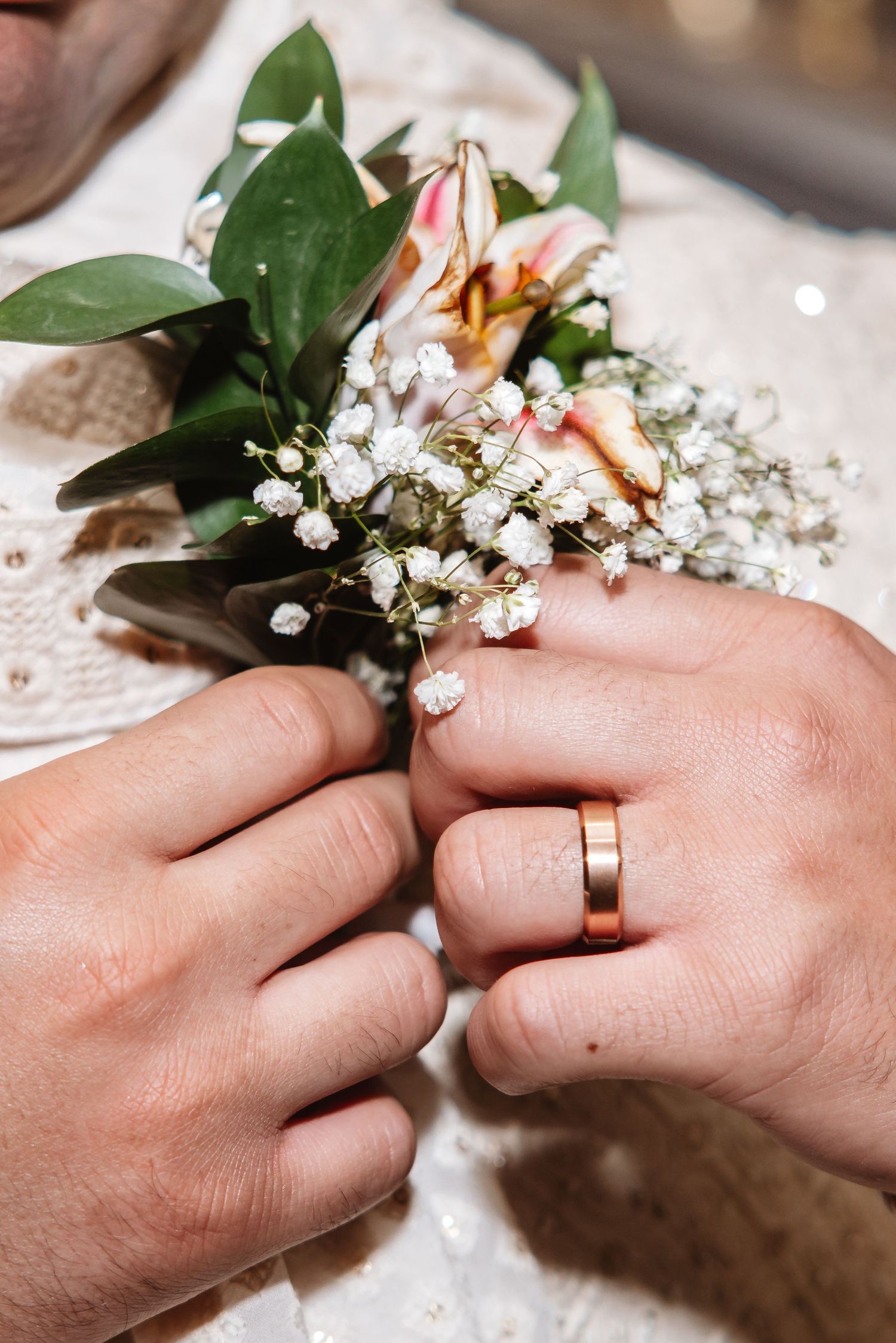 Close-up of hands pinning floral boutonniere with gold wedding band visible.