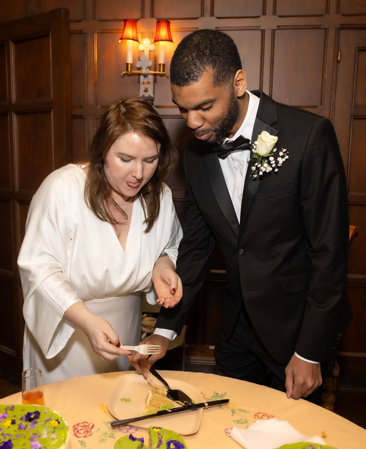Bride and groom serving wedding cake slices at a warmly lit indoor wedding reception.