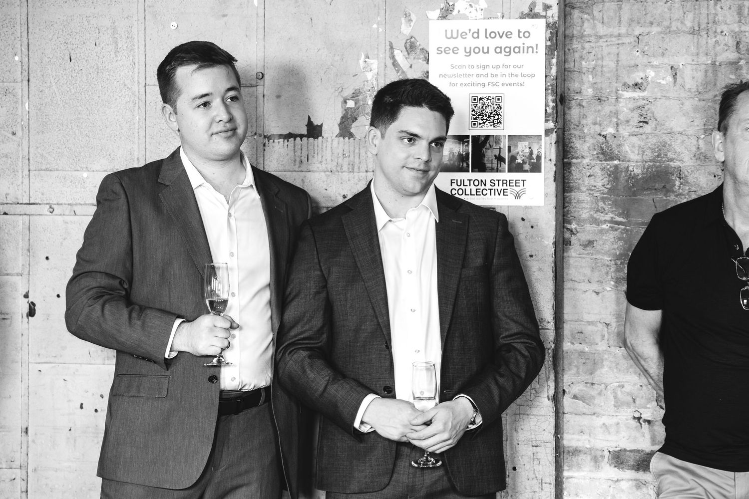 Black and white photo of two men in suits at an event near a poster.
