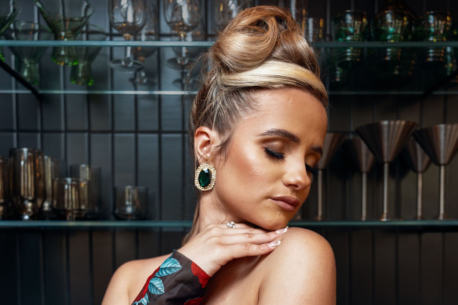 Close-up portrait of blonde woman with updo wearing green drop earring at a bar.