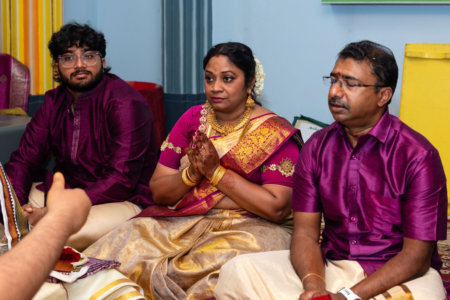 South Indian family participating in a Hindu puja ceremony wearing traditional silk saree and kurta.