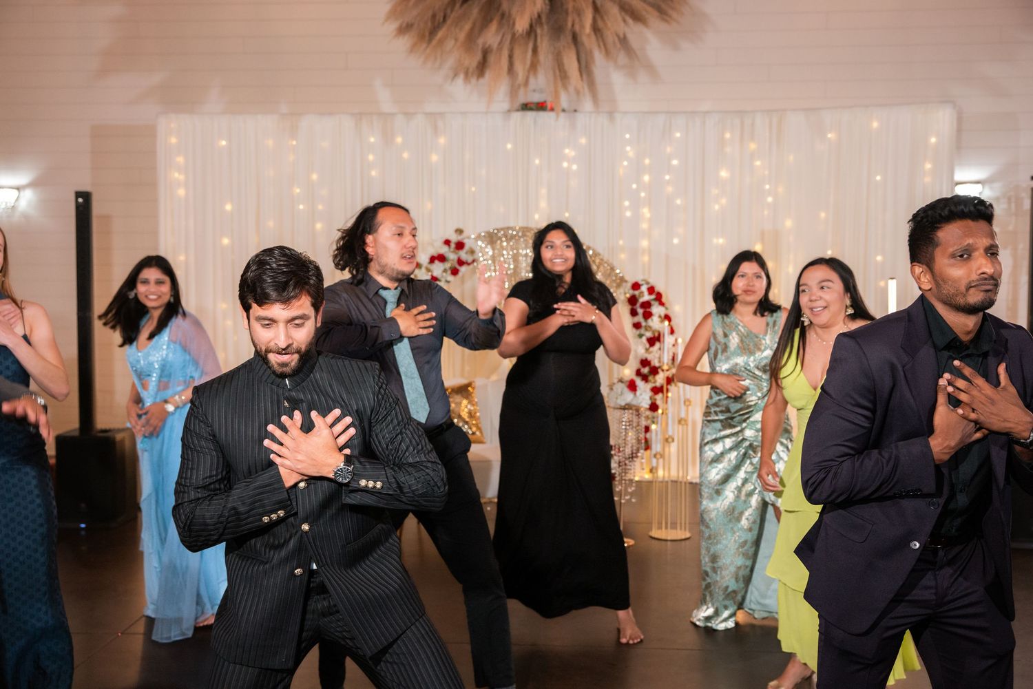 Guests dancing energetically at an Indian wedding reception with fairy light backdrop.