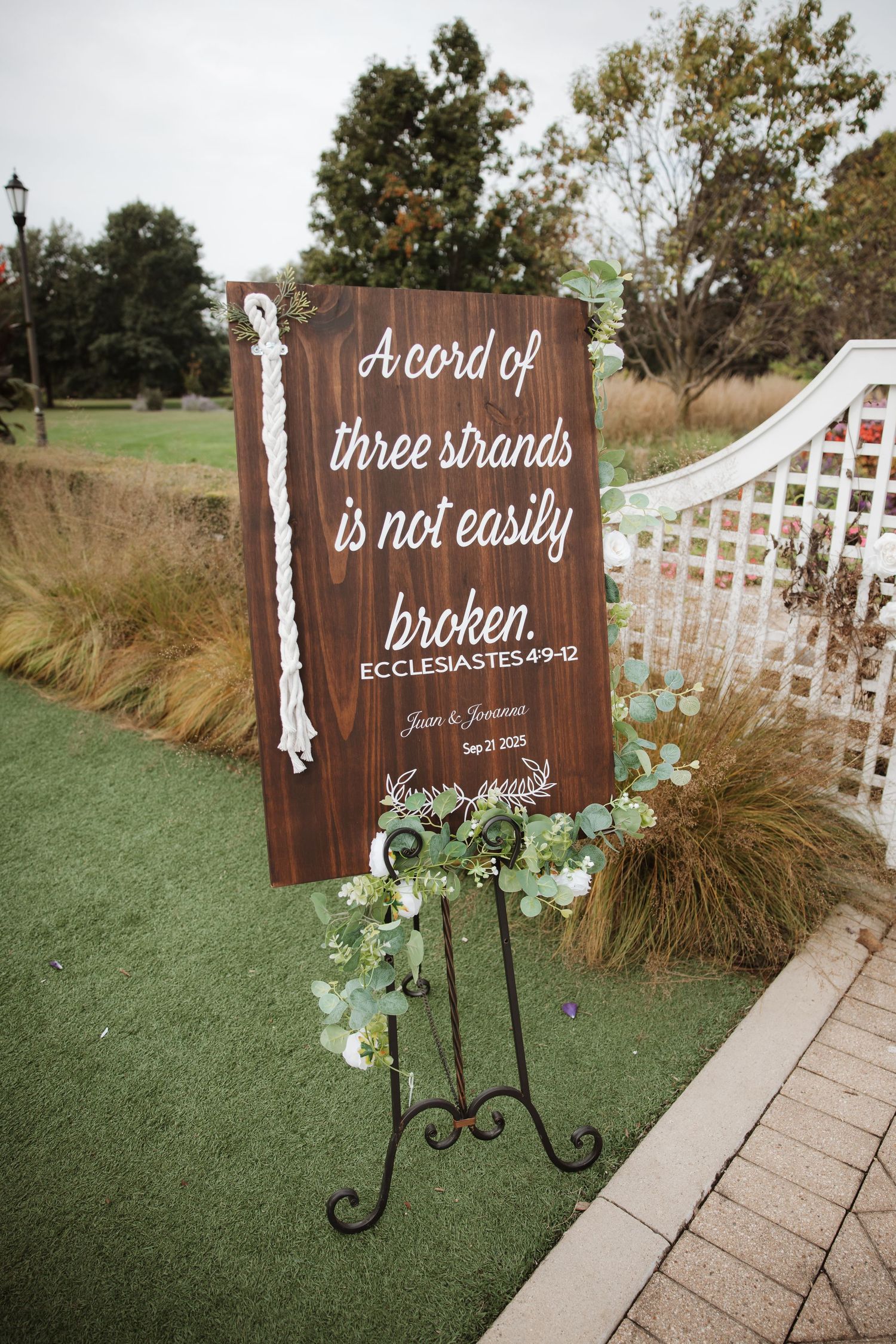 Rustic wooden wedding sign reading A Cord of Three Strands is Not Easily Broken Ecclesiastes 4:9-12 on iron easel.