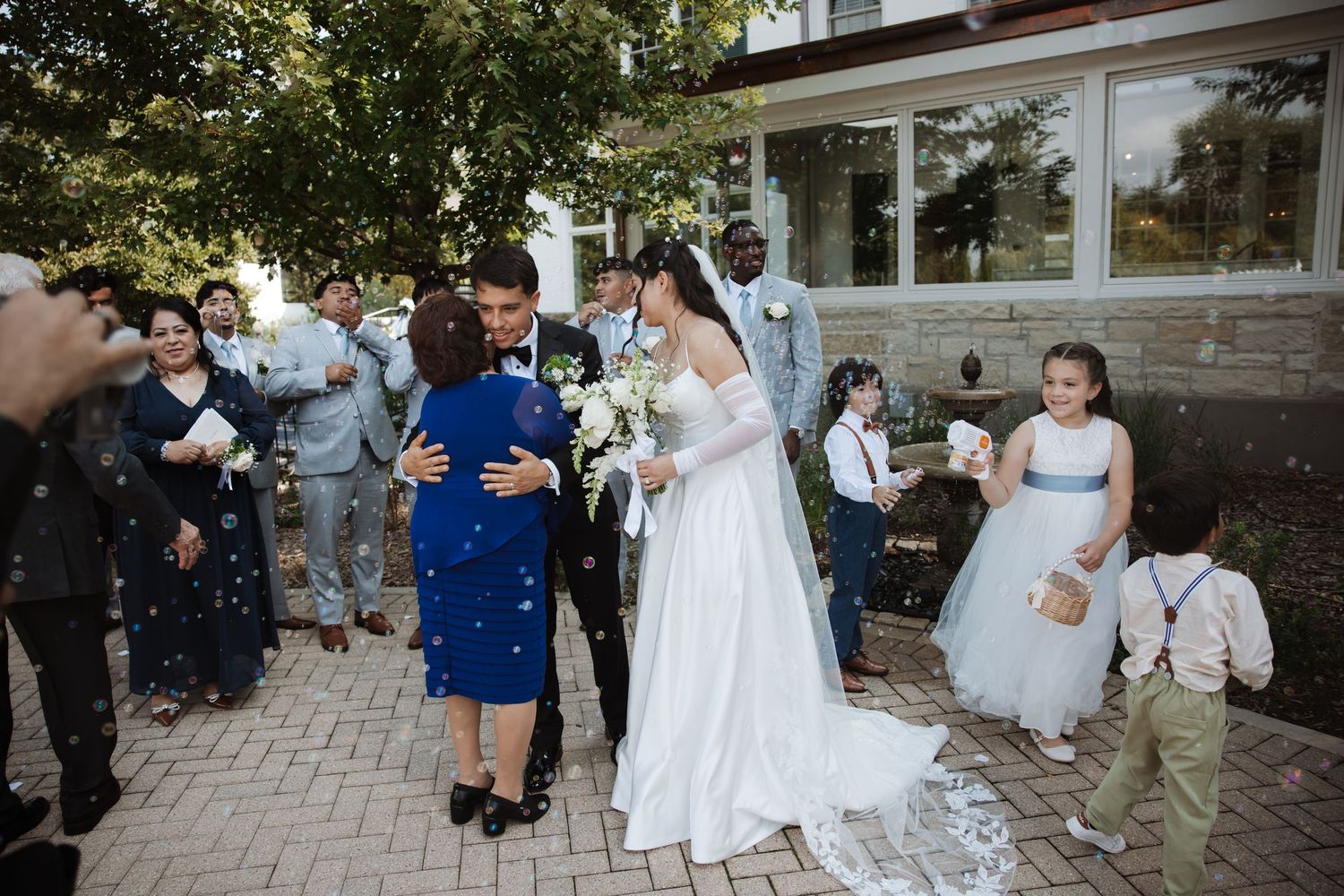 Bride and groom being greeted by guests with confetti outside a wedding venue with flower girl nearby.