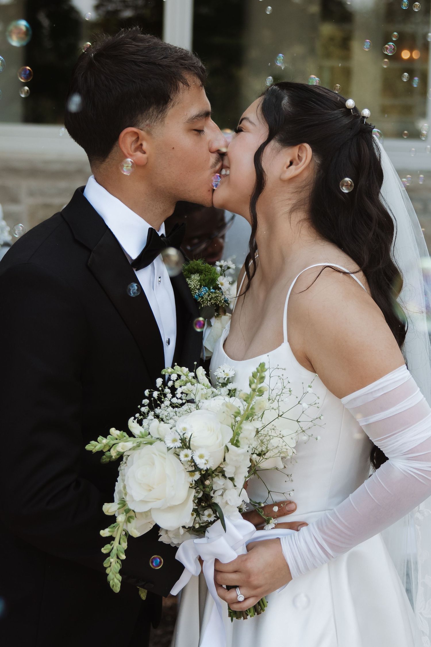 Close-up of bride and groom sharing a tender kiss surrounded by floating bubbles, bride holding white bouquet.