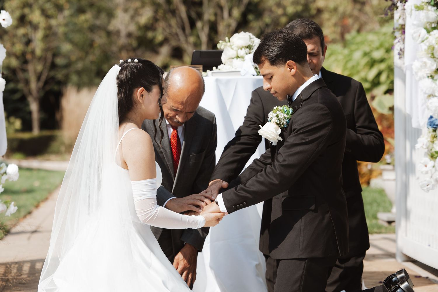 Officiant guides bride and groom during ring exchange ceremony at outdoor wedding altar.