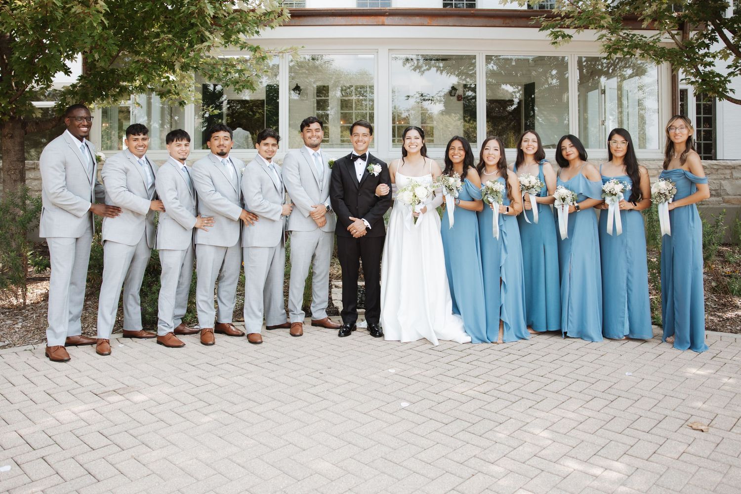 Wedding party poses together, groomsmen in gray suits and bridesmaids in blue dresses flanking bride and groom.