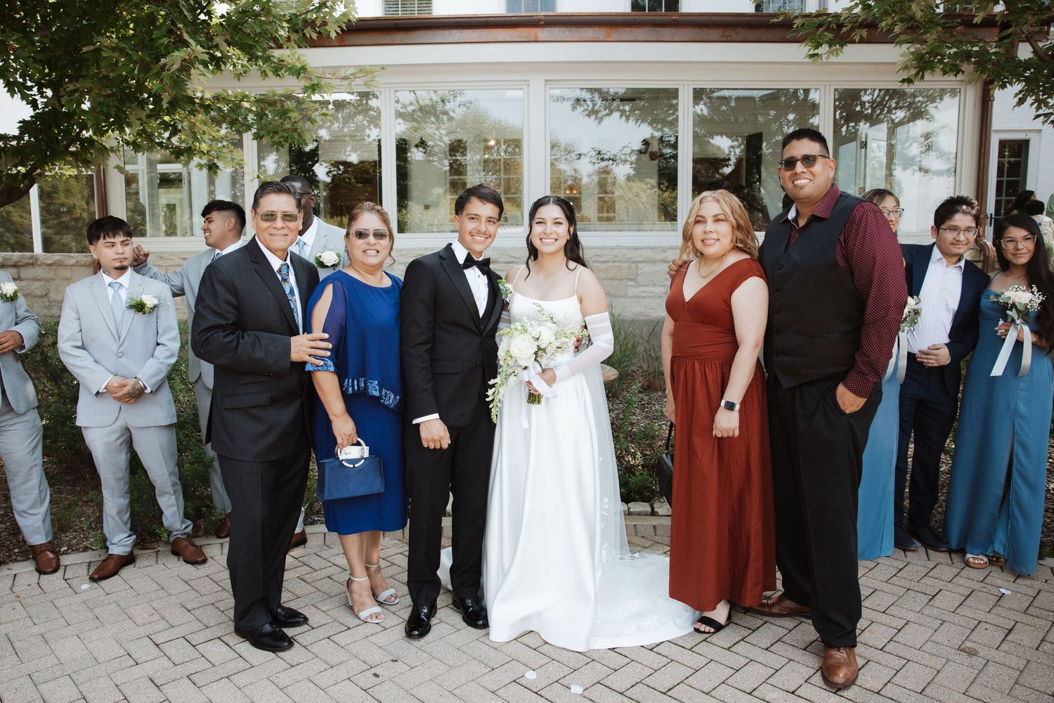 Bride and groom pose with four family members in formal attire outside wedding venue.