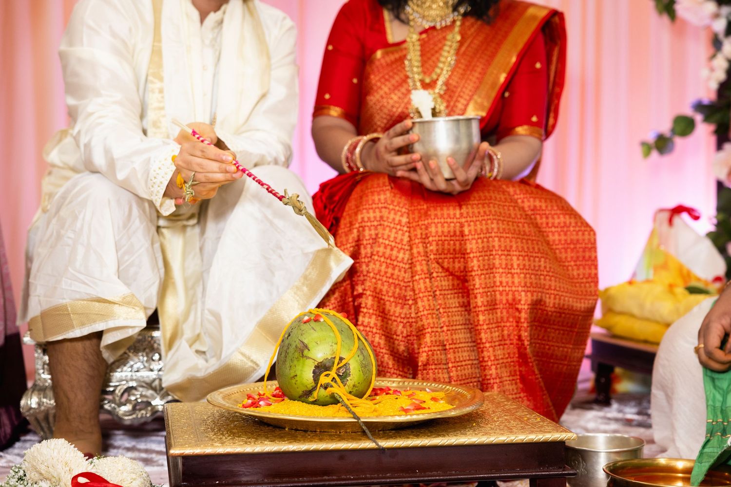 Indian wedding couple performing traditional ritual with coconut offering on decorated plate during Hindu ceremony.