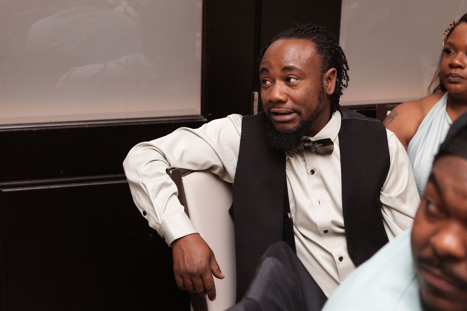 Smiling man in black vest and bow tie relaxing at a wedding reception event.