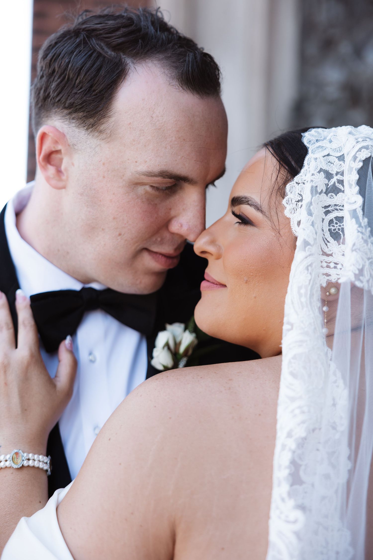 Romantic close-up of bride and groom nearly kissing, bride wearing intricate lace mantilla wedding veil.