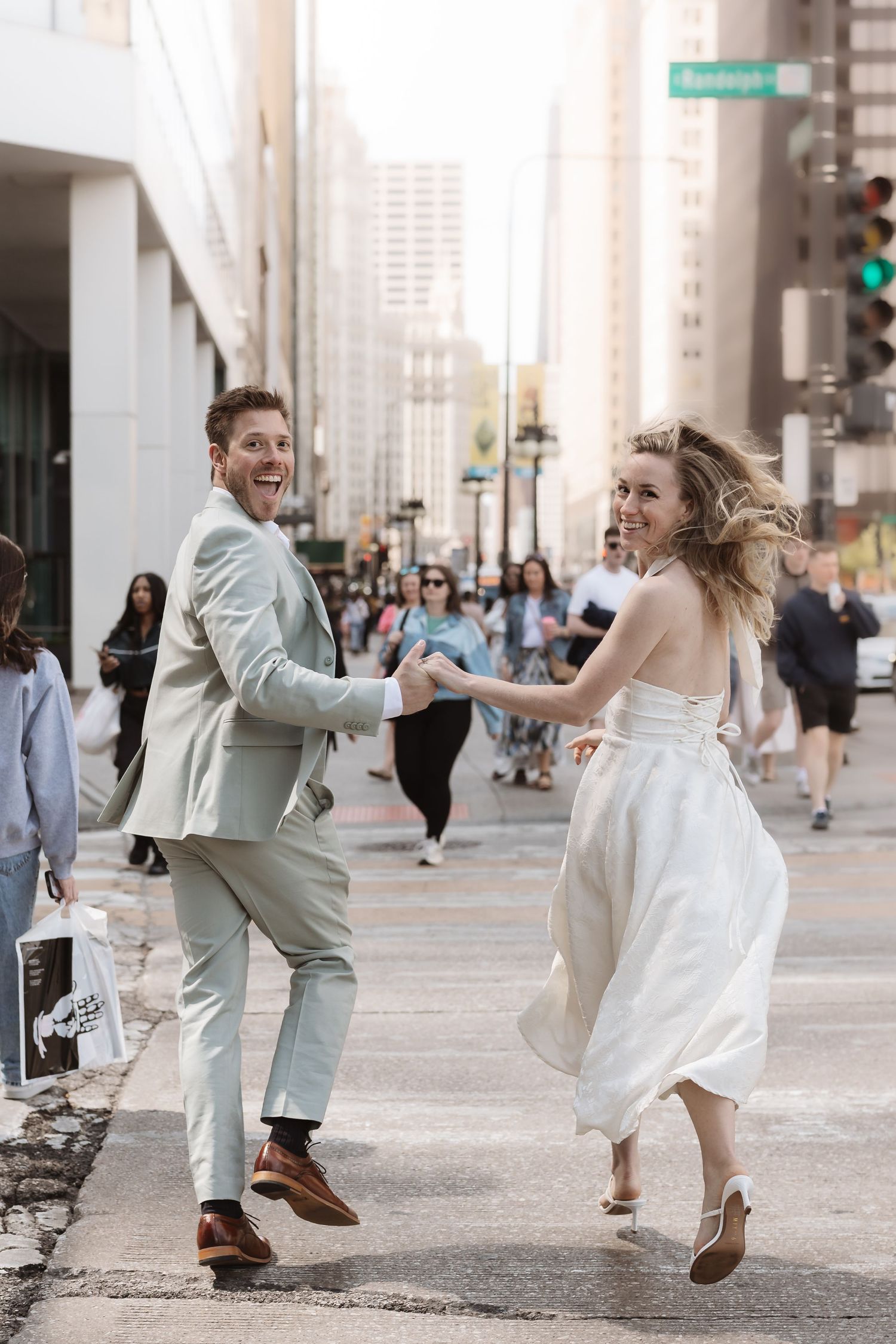 Bride and groom hold hands dancing joyfully on a busy city street.