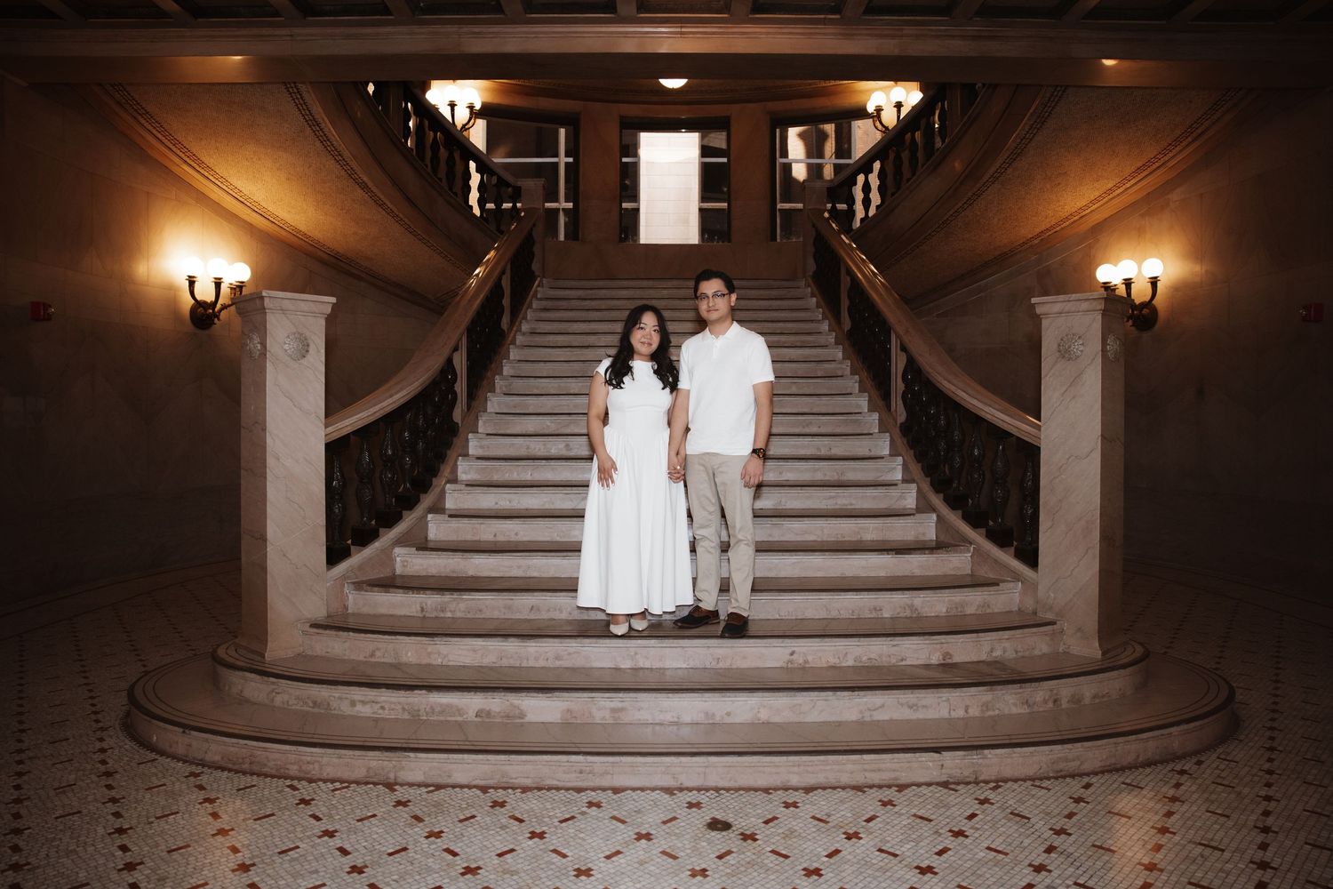 Engaged couple stands together at the base of an elegant grand staircase in a historic Chicago building.