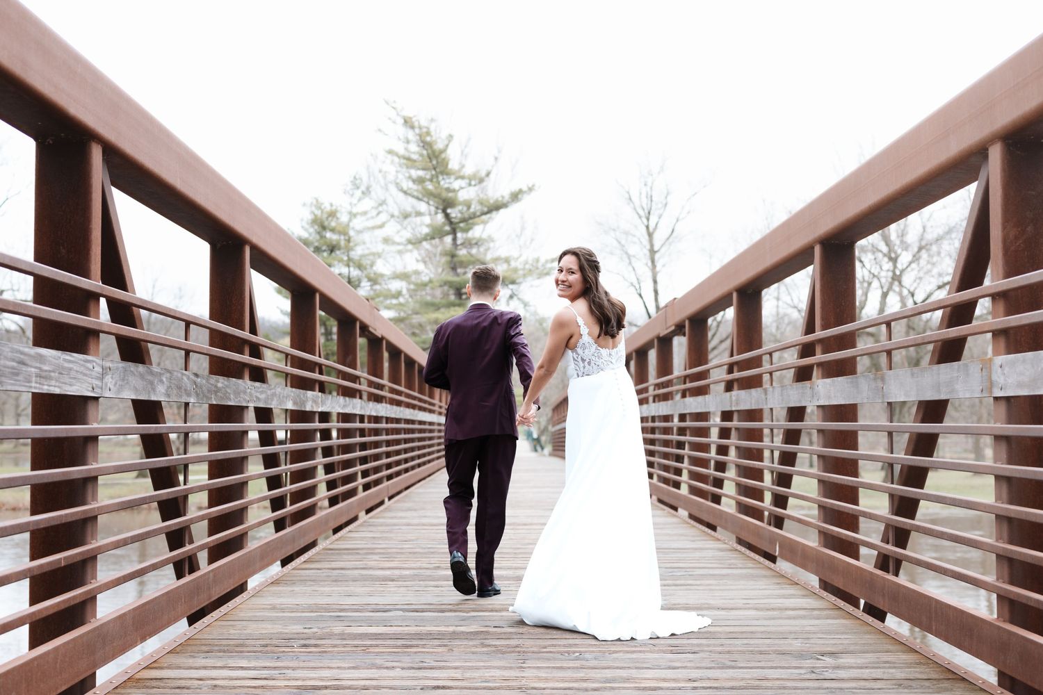 Bride and groom walking hand in hand on a wooden bridge on their wedding day.