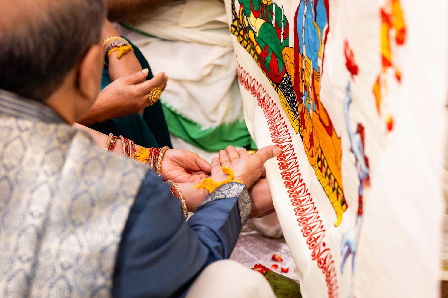 Close-up of Hindu wedding ritual with turmeric ceremony being performed on bride and groom's hands.
