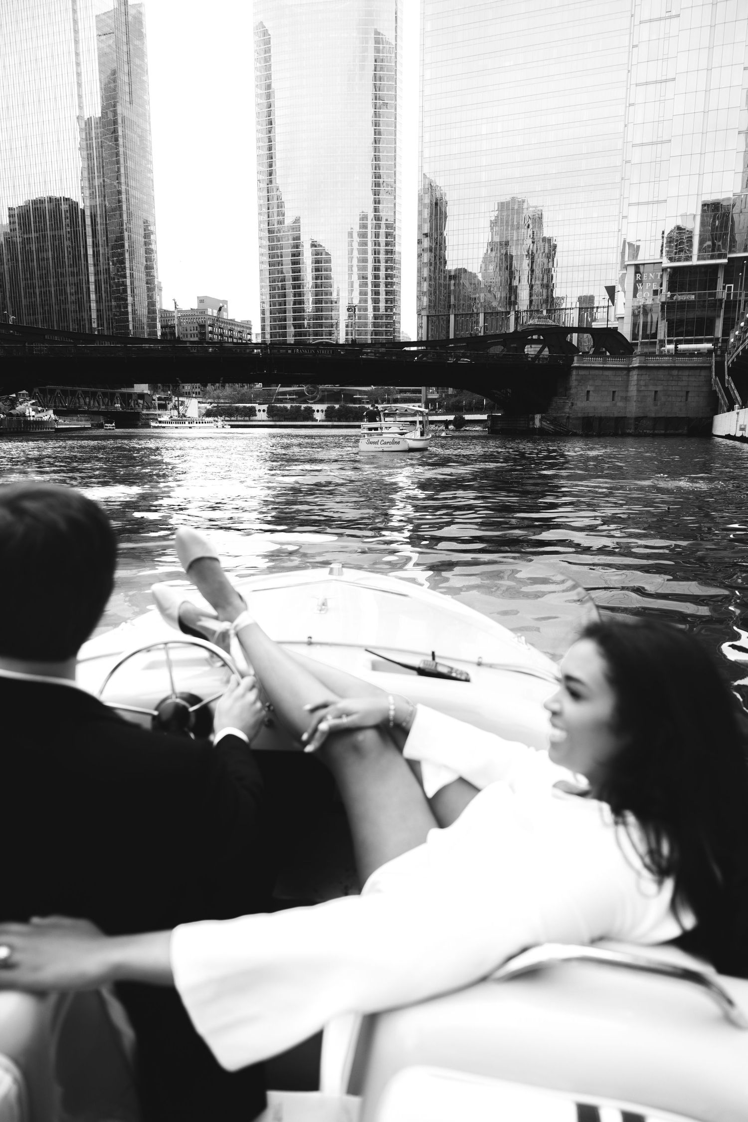Black and white photo of couple in a speedboat on Chicago river with city skyline in background.