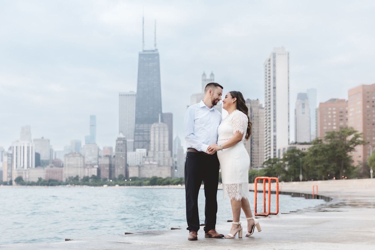 Couple posing on Chicago lakefront with city skyline and John Hancock Center in background.