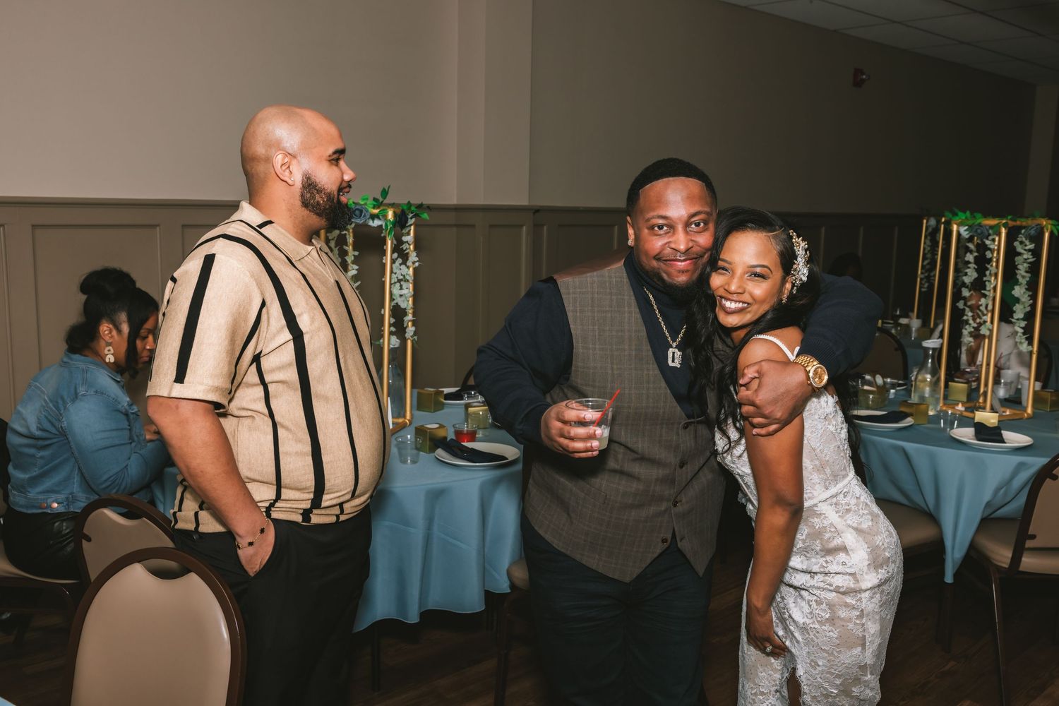 Three guests share a joyful moment at an elegant wedding reception with blue table settings in the background.