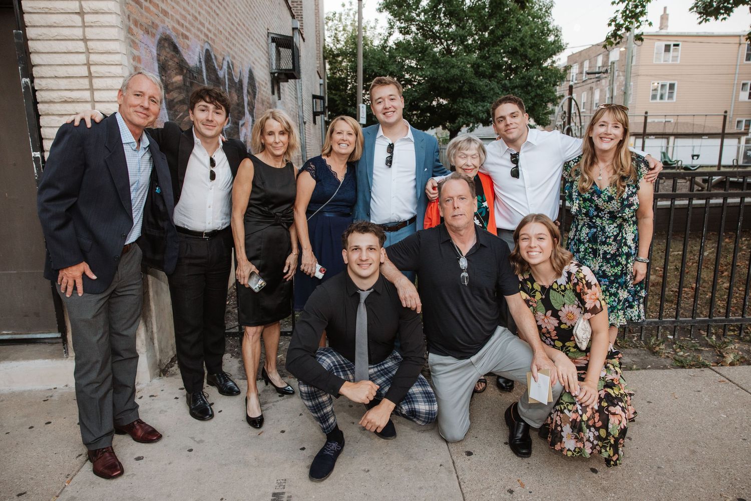 Smiling extended family group photo taken outdoors on a city sidewalk during a celebration.